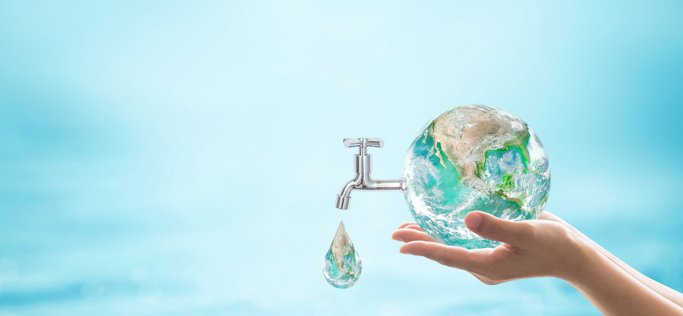 Immagine concettuale che mostra due mani che sorreggono con cura un globo terrestre trasparente. Da un lato del globo emerge un rubinetto cromato da cui cade una singola goccia d'acqua, la quale contiene al suo interno un riflesso della Terra. Lo sfondo è azzurro chiaro e sfocato.