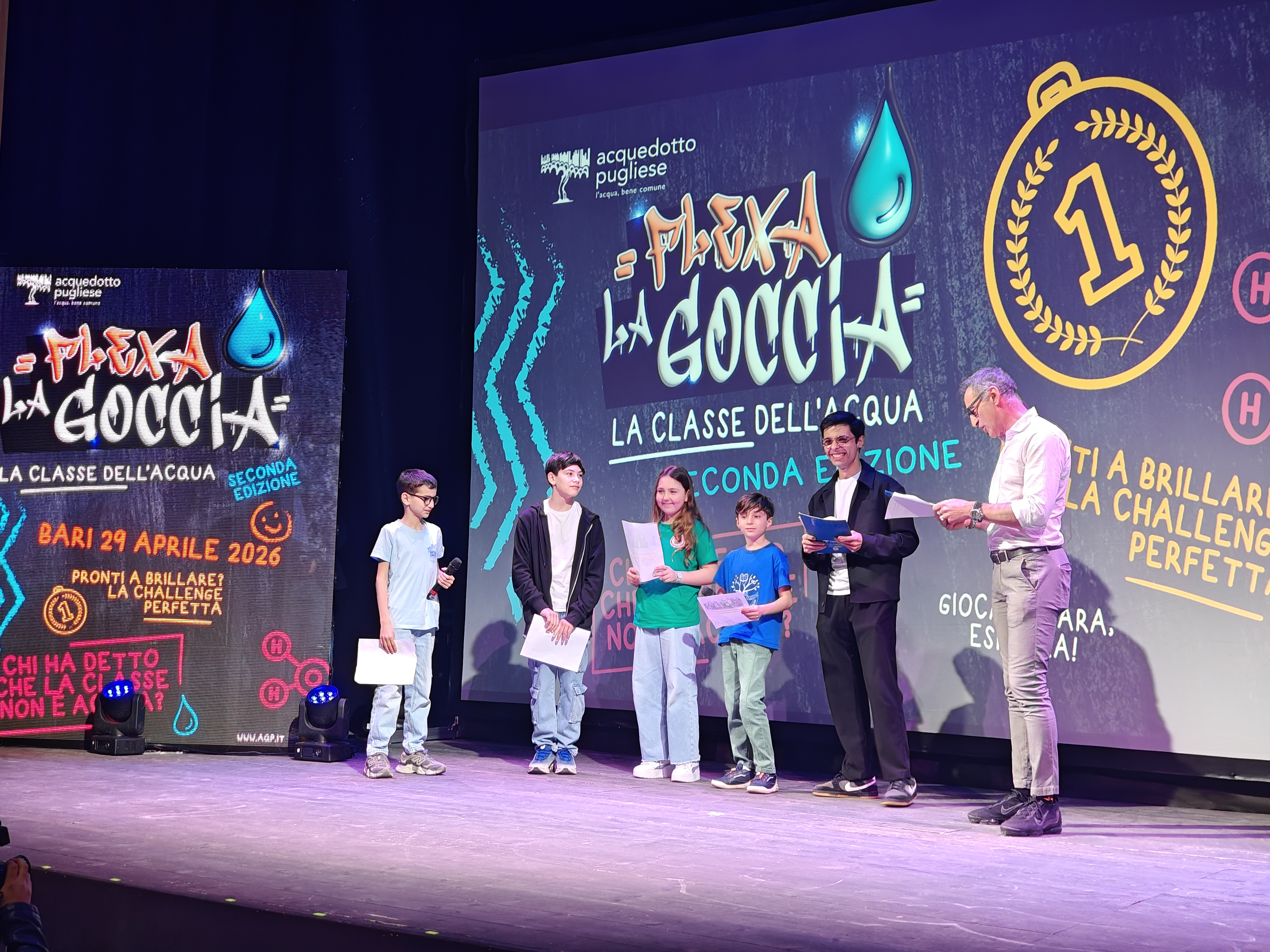Una foto del palcoscenico con il collega Vito Palumbo, Nick Radogna e alcuni bambini delle scuole partecipanti foto allo schermo con la proiezione di un video