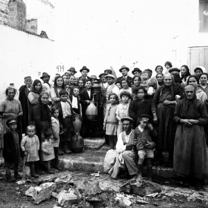 Una fotografia d'epoca in bianco e nero ad alta densità di soggetti, che mostra la comunità locale radunata attorno a una fontana pubblica.
